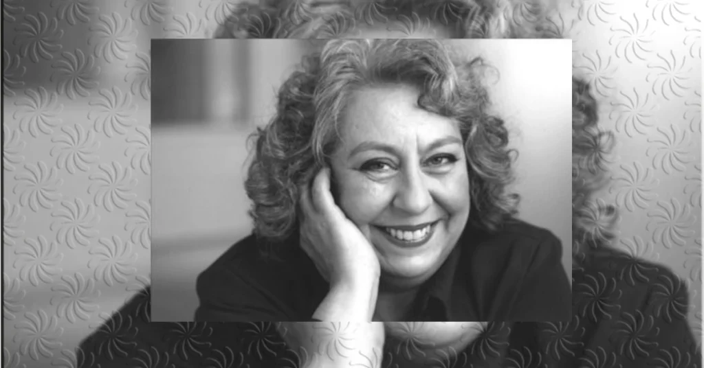 Portrait of a woman with curly gray hair smiling while resting her face on her hand